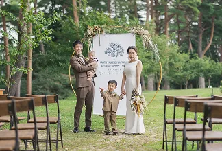 屋外の結婚式で、幼い子供を笑顔で抱きかかえる新郎新婦。