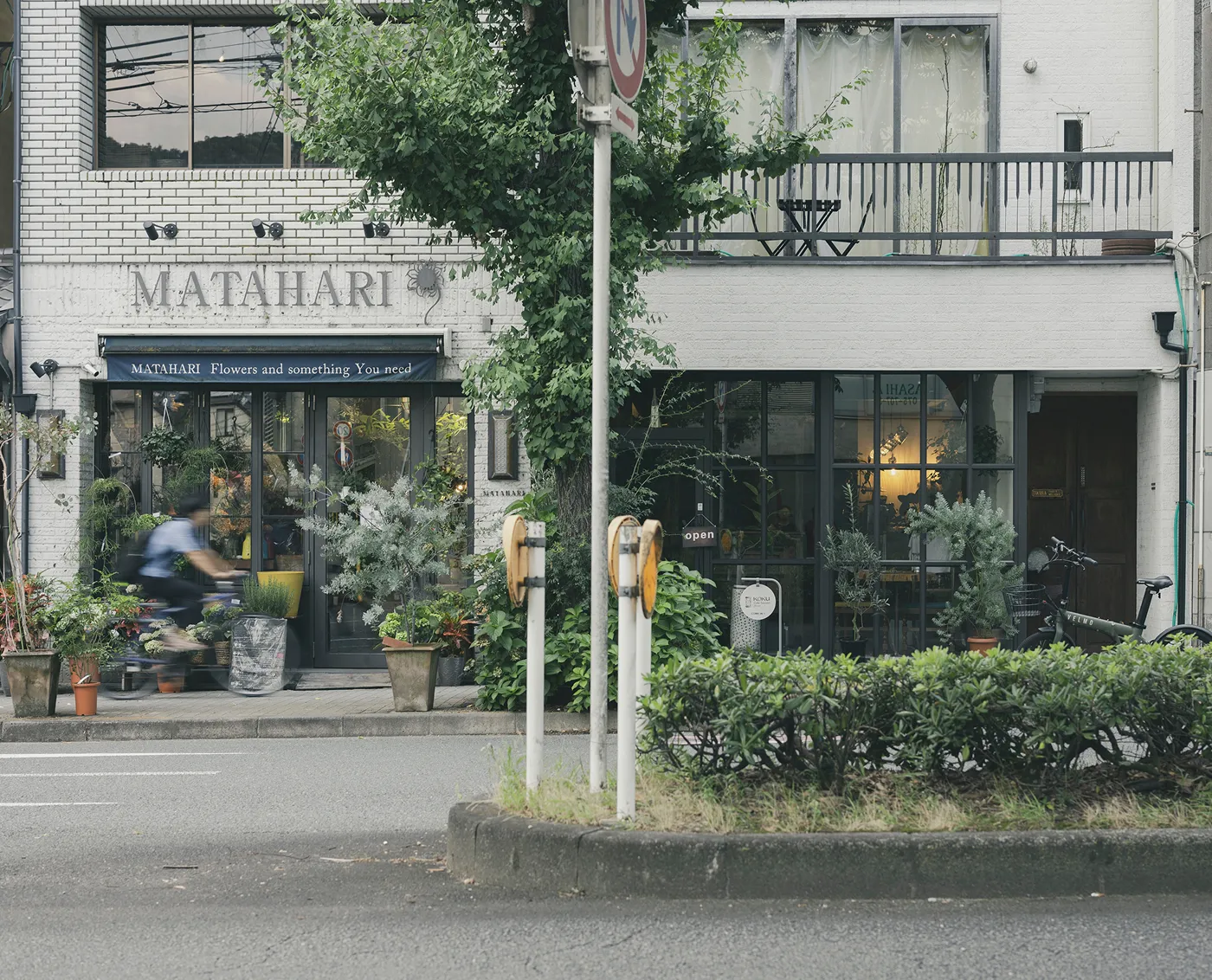 緑豊かな街路樹の前に立つ、おしゃれなフラワーショップの店構え。